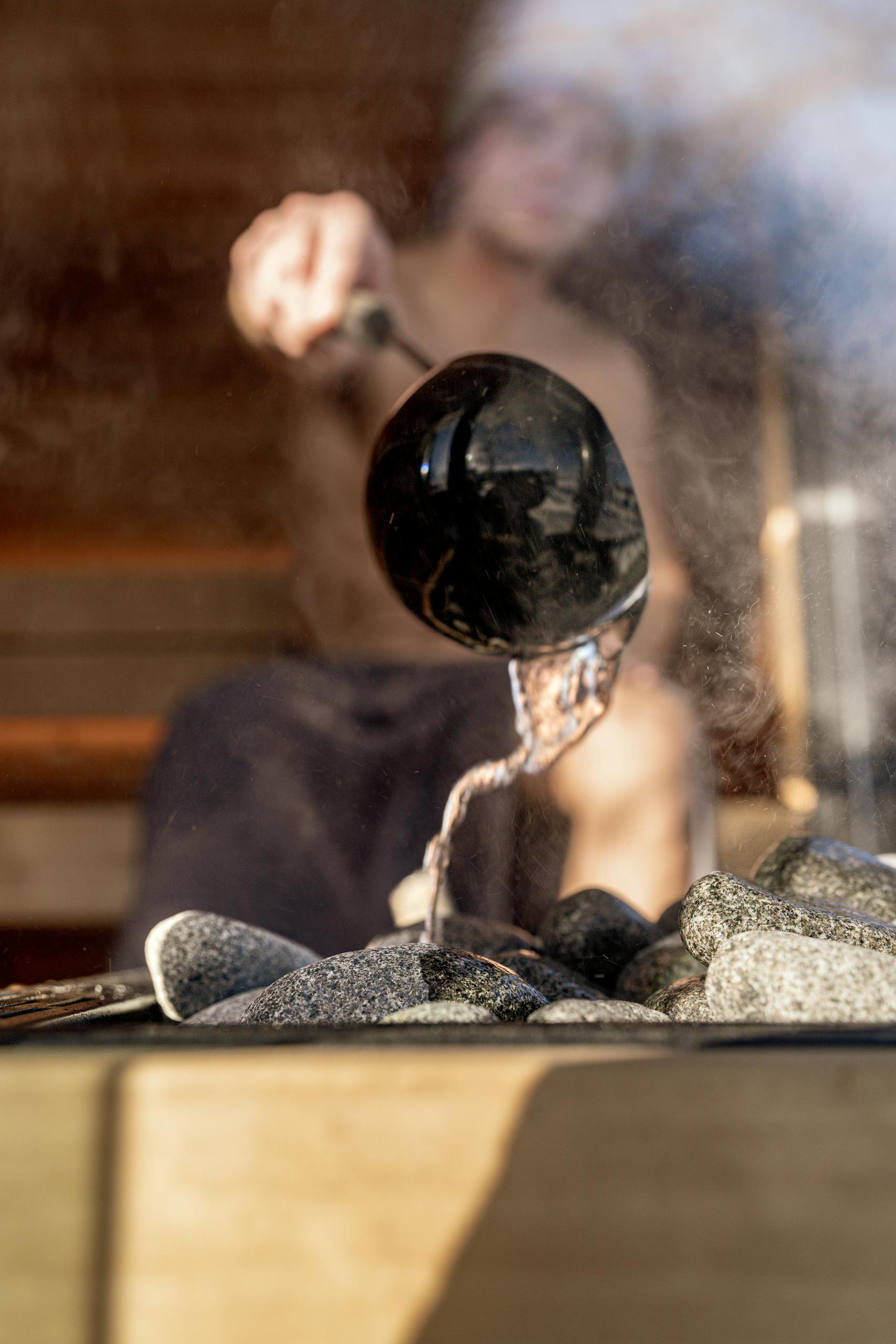 A close-up view of water being poured over sauna stones, creating steam in a serene environment.