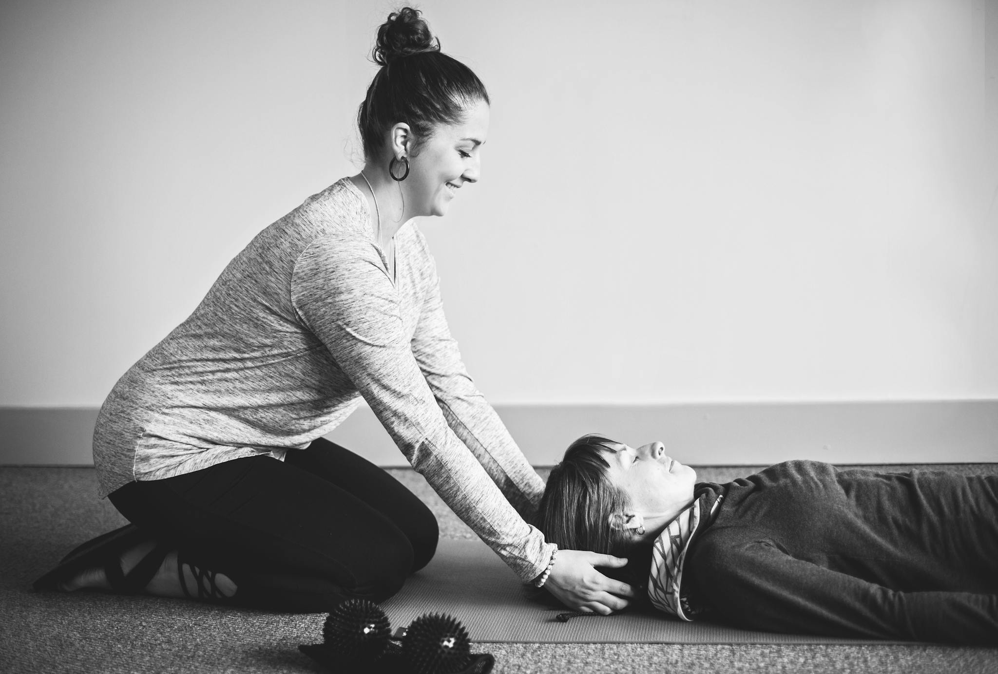 A therapist provides a relaxation session to a client lying on a mat indoors.